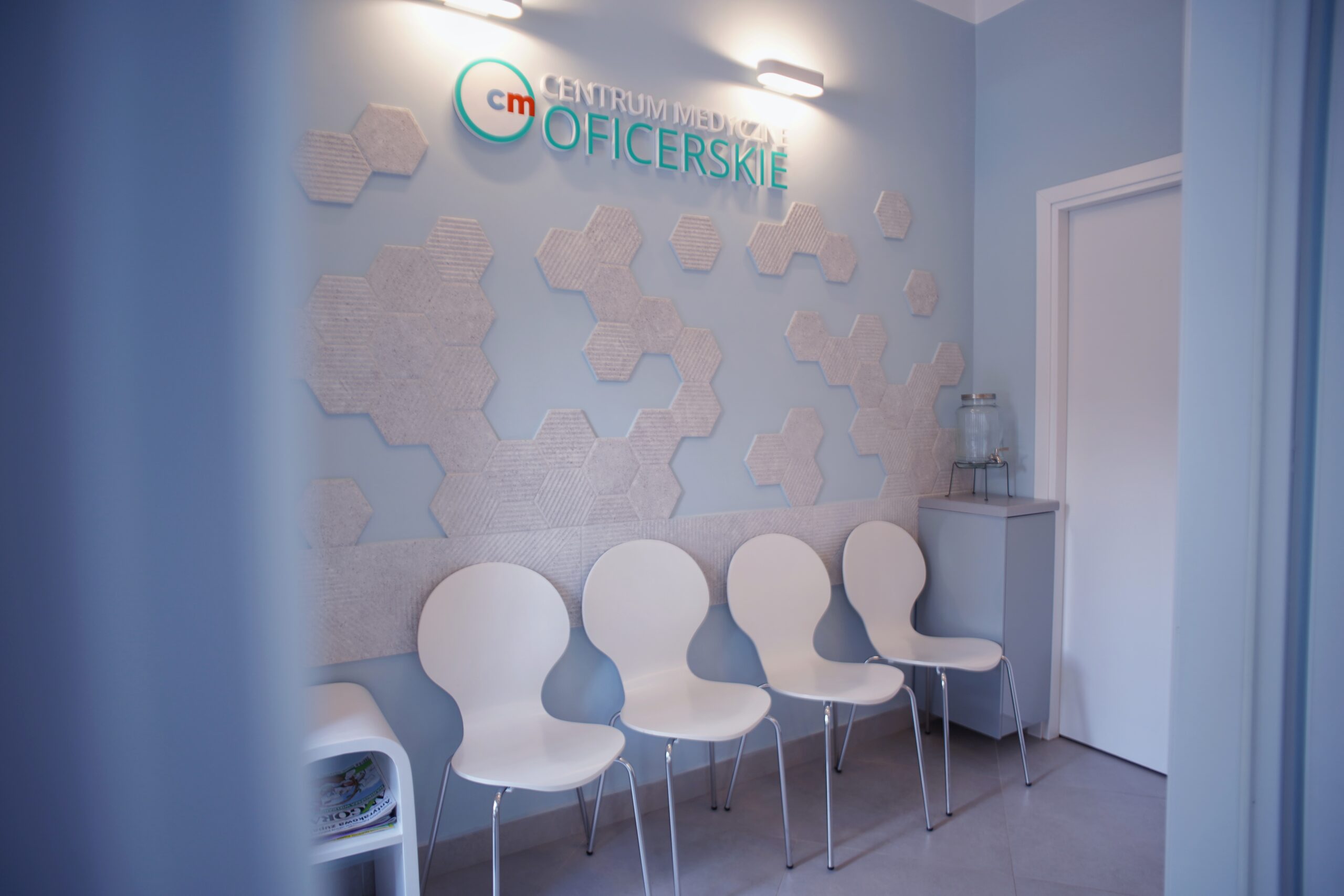 Przestronna poczekalnia Centrum Medycznego Oficerskie — jasne wnętrze z białymi krzesłami i panelami akustycznymi